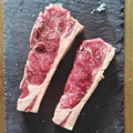 Two raw irish moiled sirloin steaks on a slate board with a wooden background