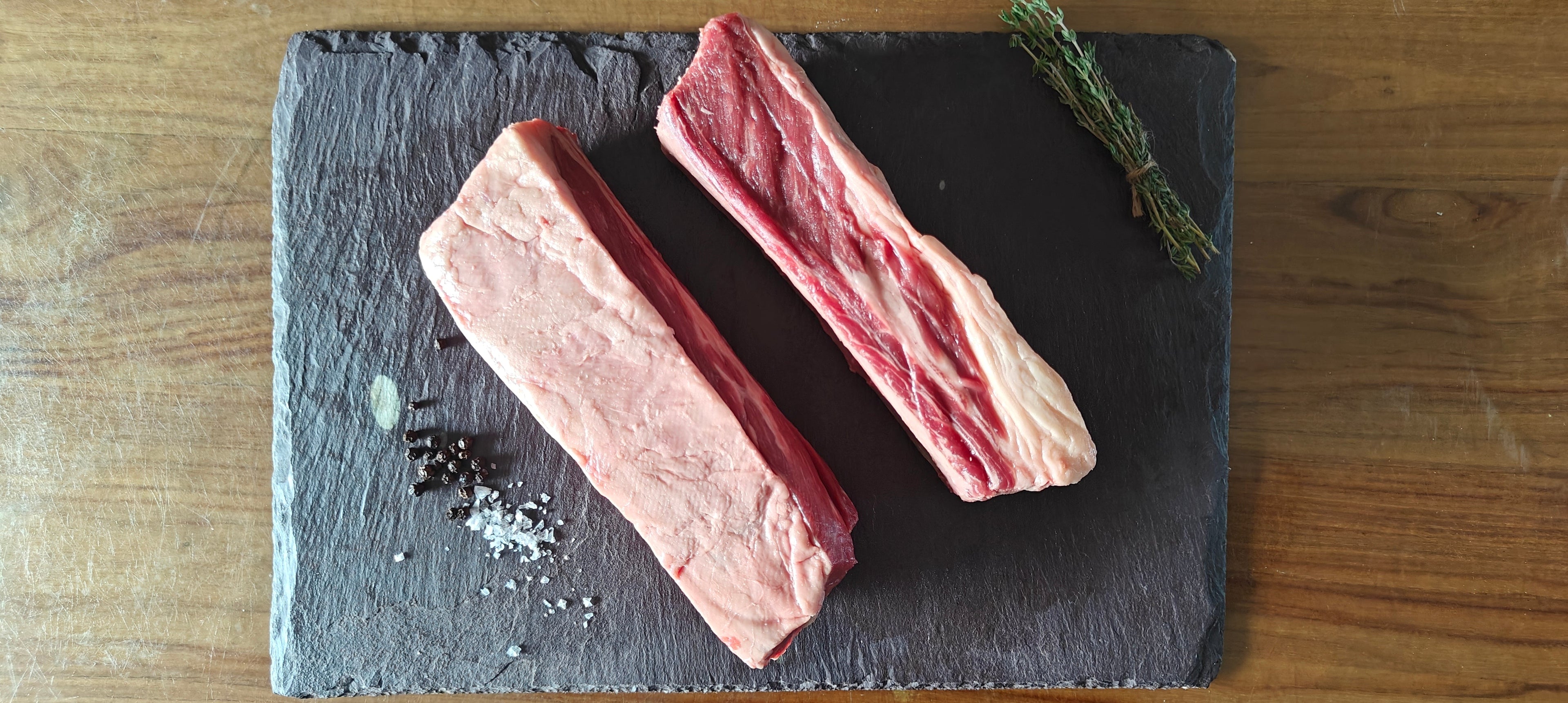 Two irish moiled short rib on a slate board with herbs and spices on a wooden surface
