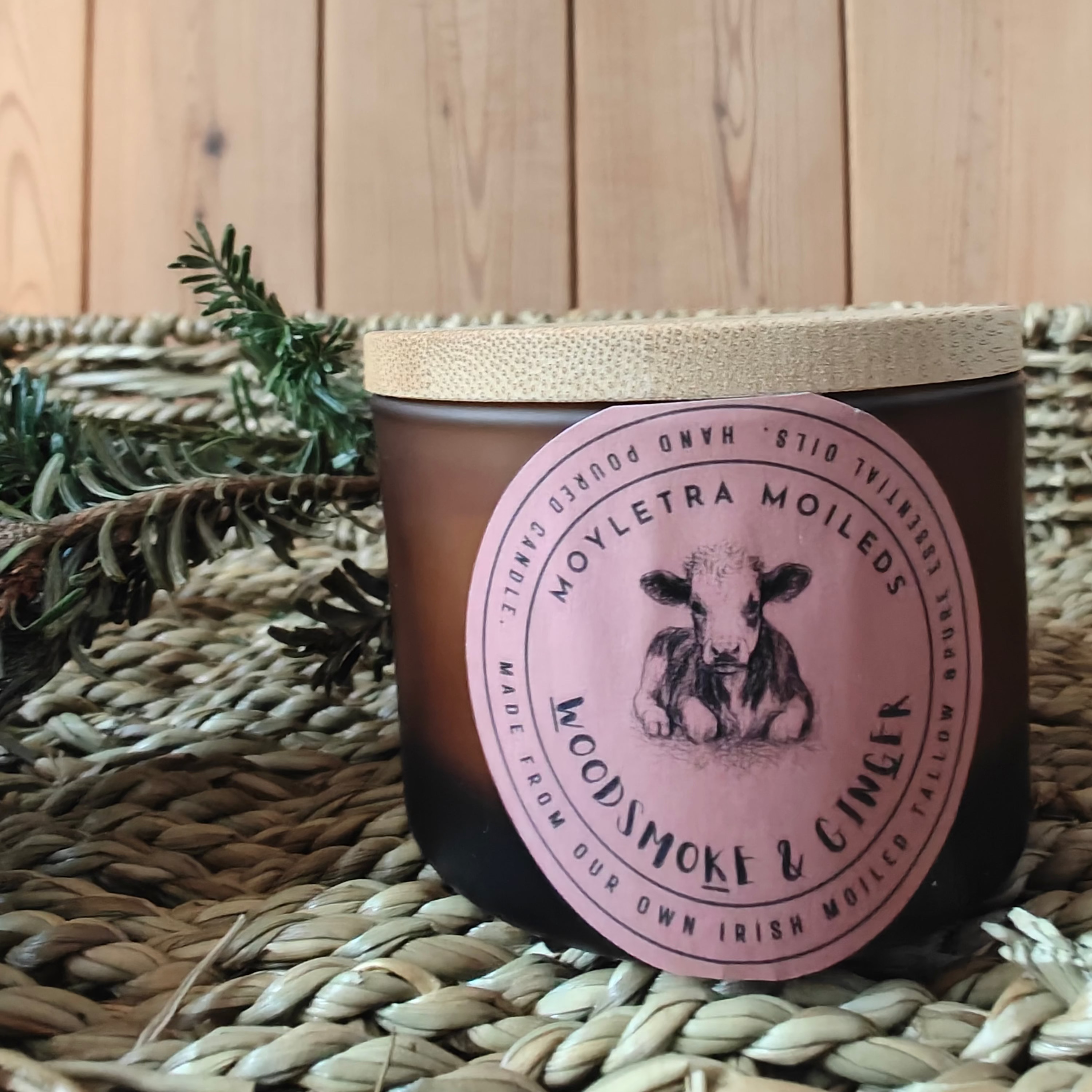 woodsmoke and ginger tallow candle with a pink label, brown glass jar and wicker background.