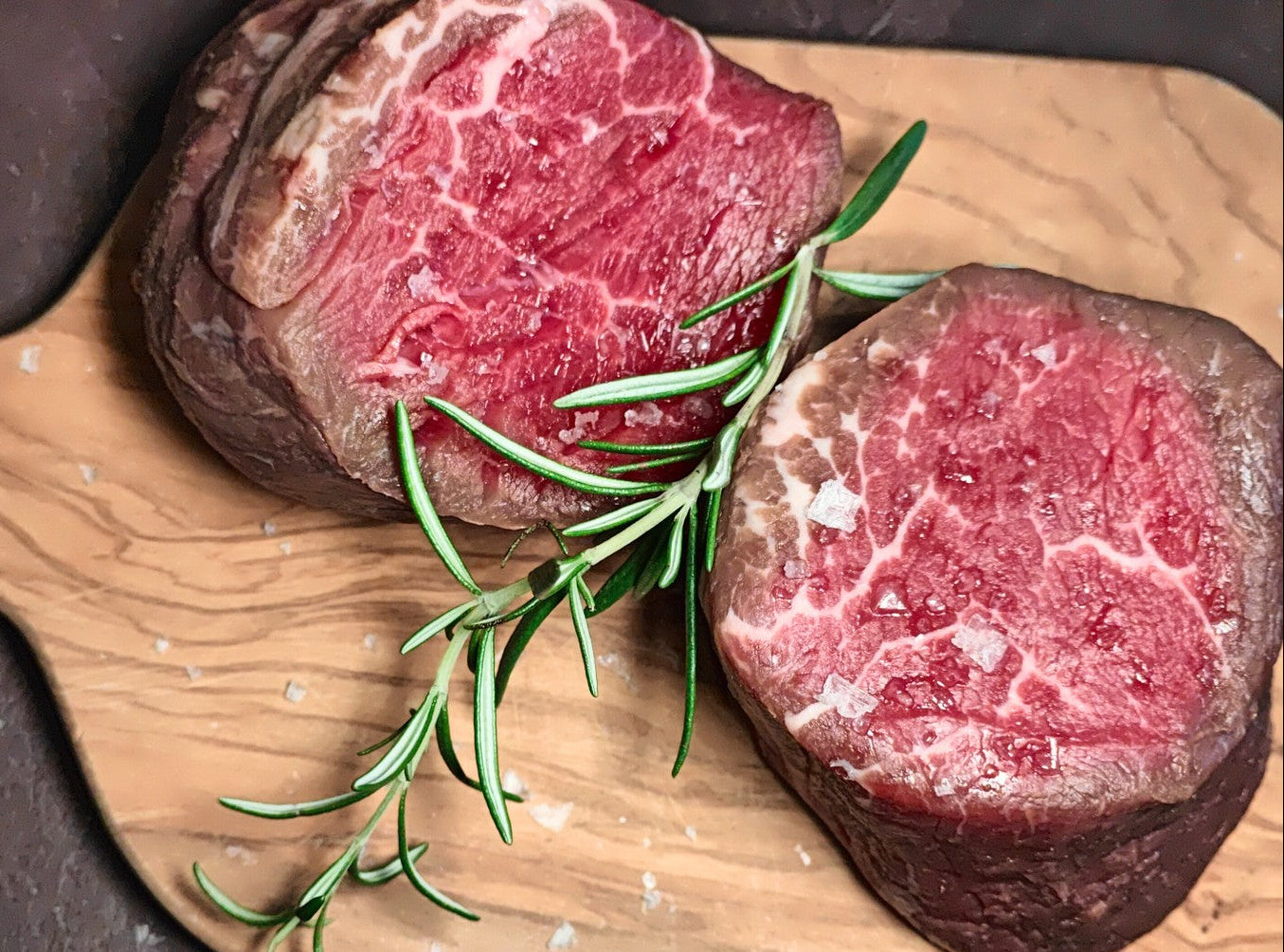 Raw irish moiled beef steaks on a wooden cutting board with rosemary