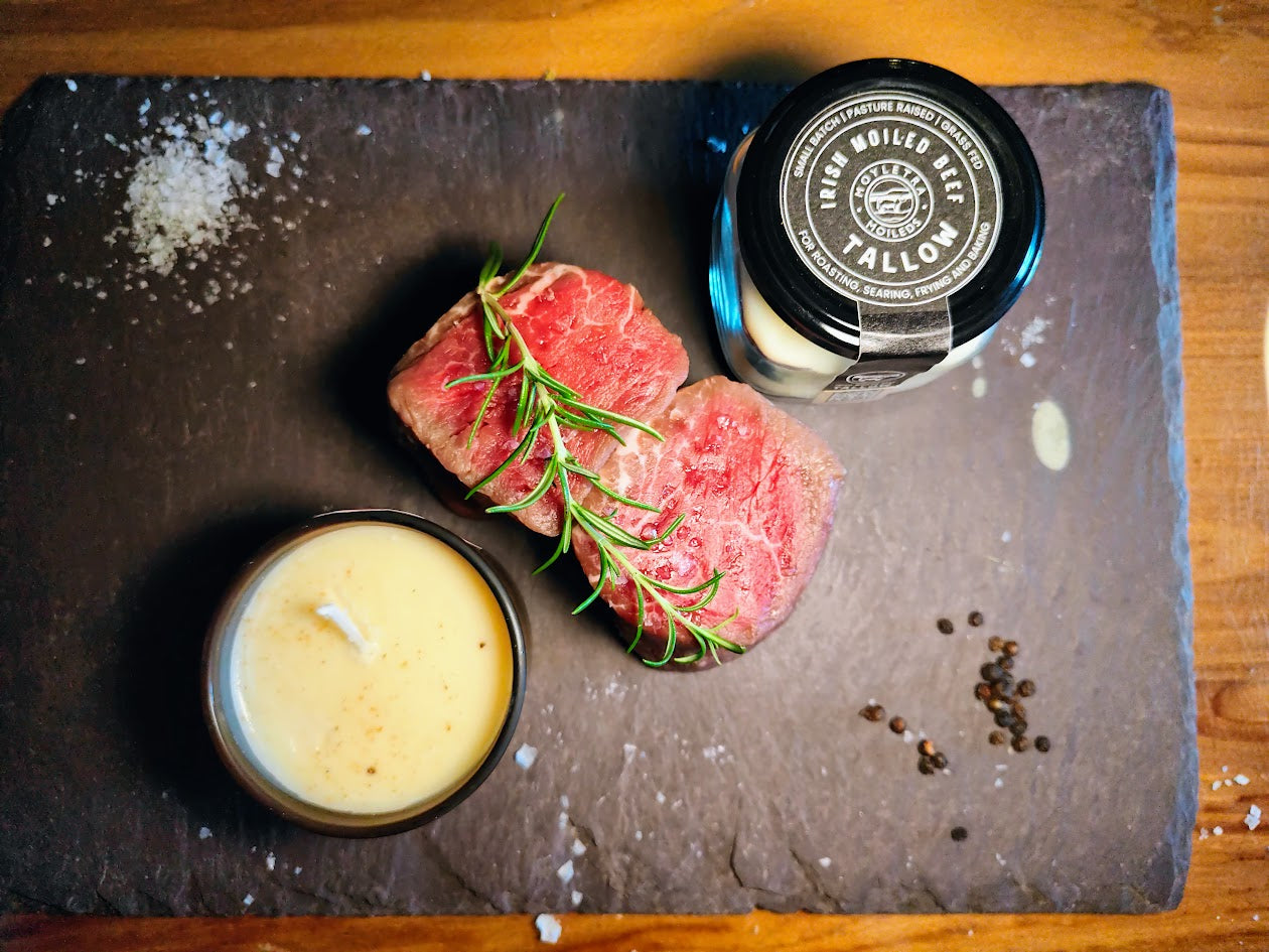 Raw beef steaks with a candle and a tallow jar on a slate board