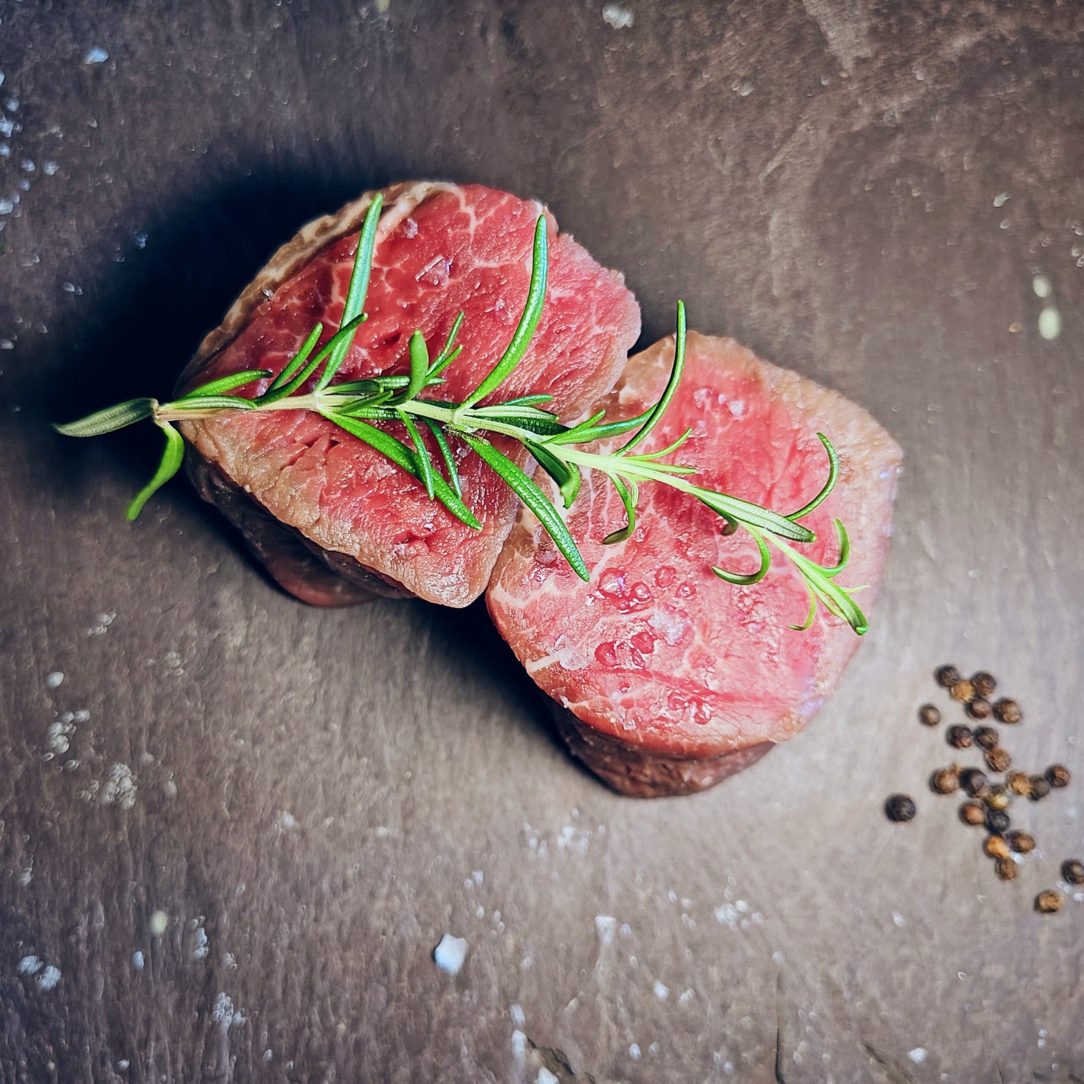Two Irish Moiled Fillet Steaks with rosemary on a dark surface