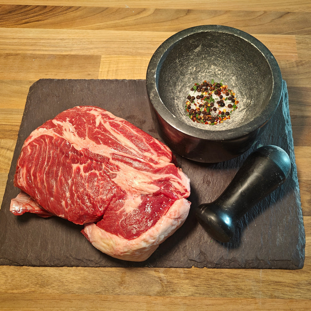 Raw steak on a stone slab with a mortar and pestle on a wooden surface
