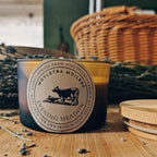 Candle with a label on a wooden surface with lavender and wicker baskets in the background