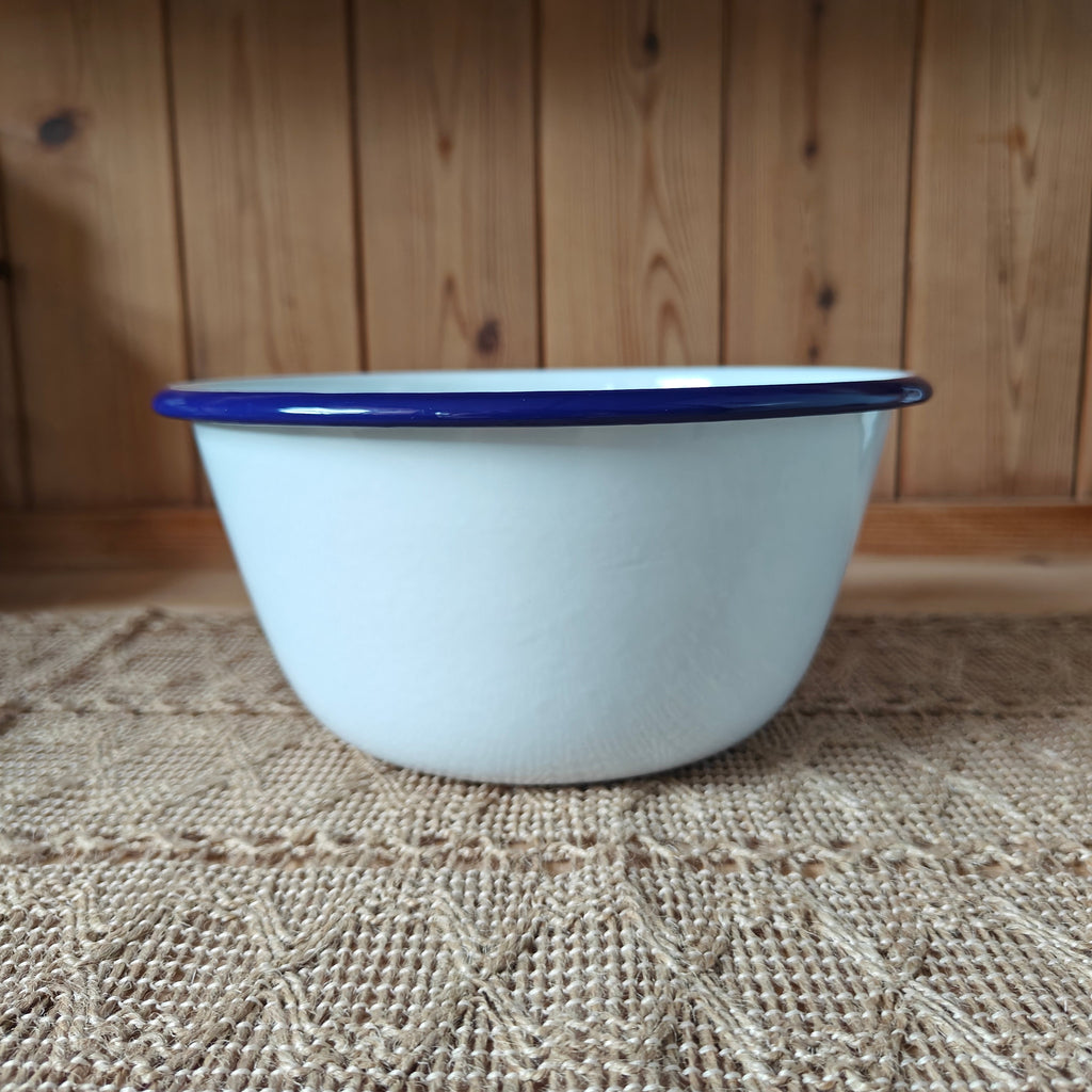White enamel basin with blue rim on a textured surface with wooden background