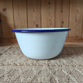 White enamel basin with blue rim on a textured surface with wooden background