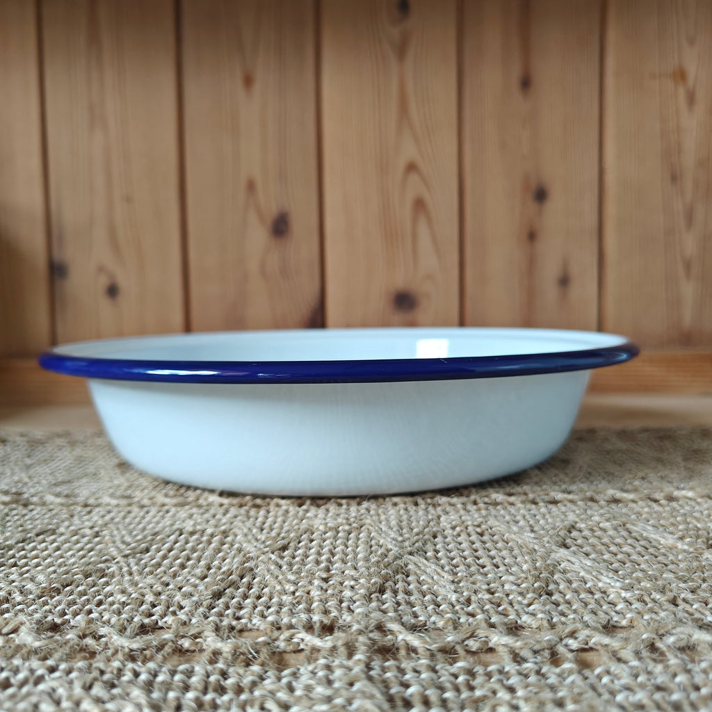 White enamel bowl with blue rim on a textured surface with wooden background