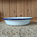 White enamel bowl with blue rim on a textured surface with wooden background