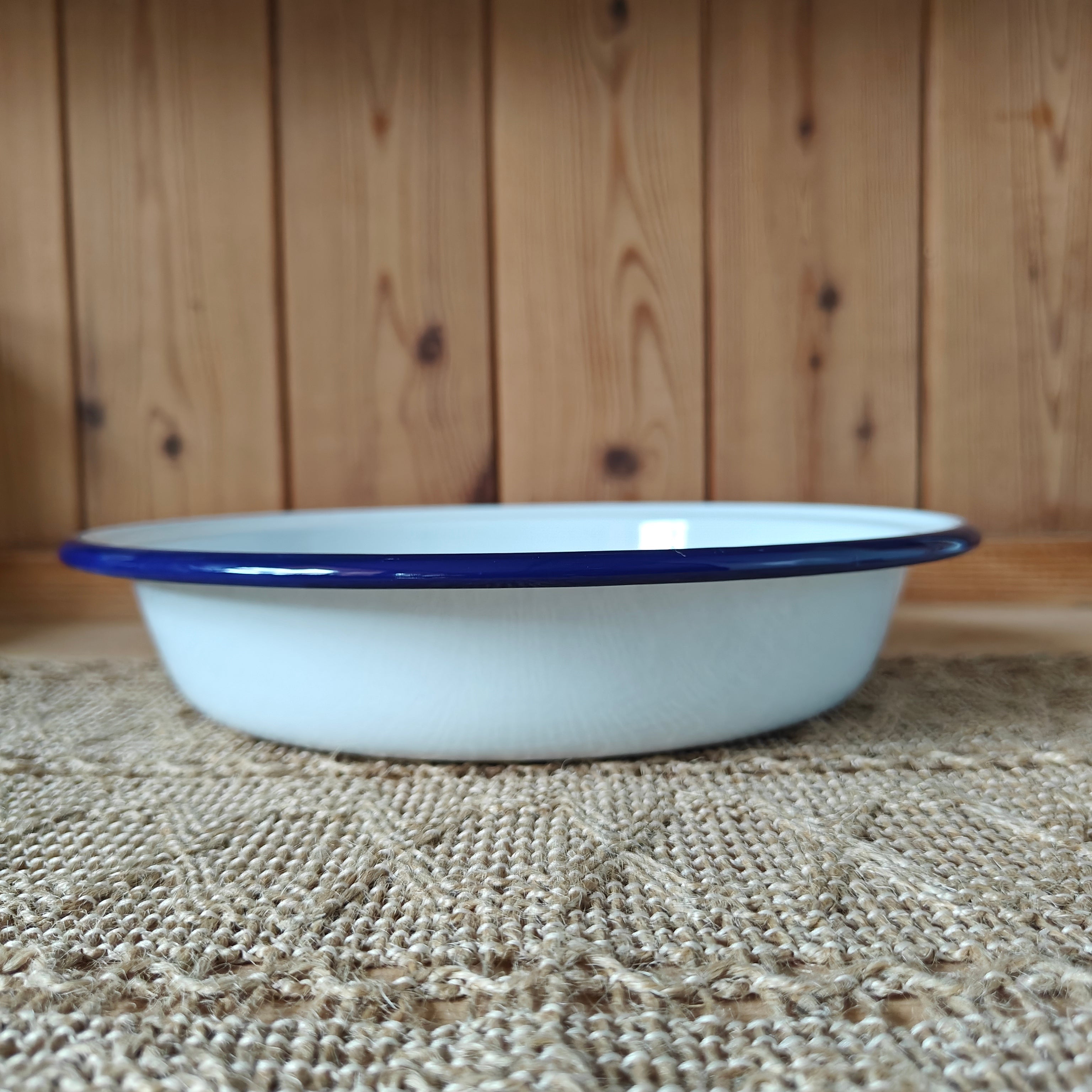 White enamel bowl with blue rim on a textured surface with wooden background