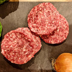Four raw hamburger patties on a dark surface with lettuce and an onion.