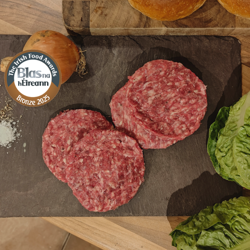 Raw irish moiled burger patties on a slate surface with an onion, bread, and lettuce, featuring the Blas na hEireann award.