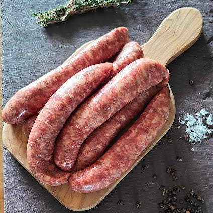 Raw sausages on a wooden board with herbs and salt on a slate surface.